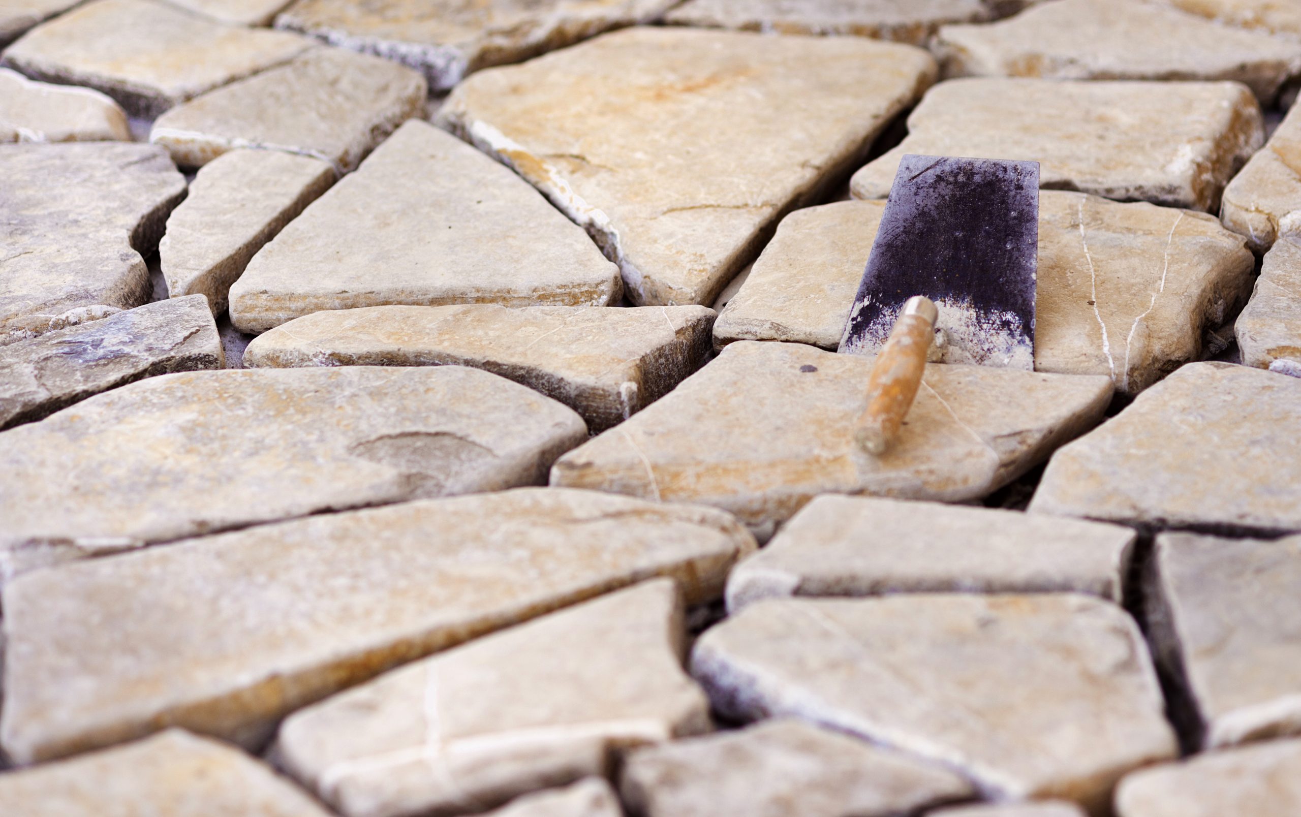 A close-up view of irregular stone slabs arranged on the ground, with a trowel resting among them.